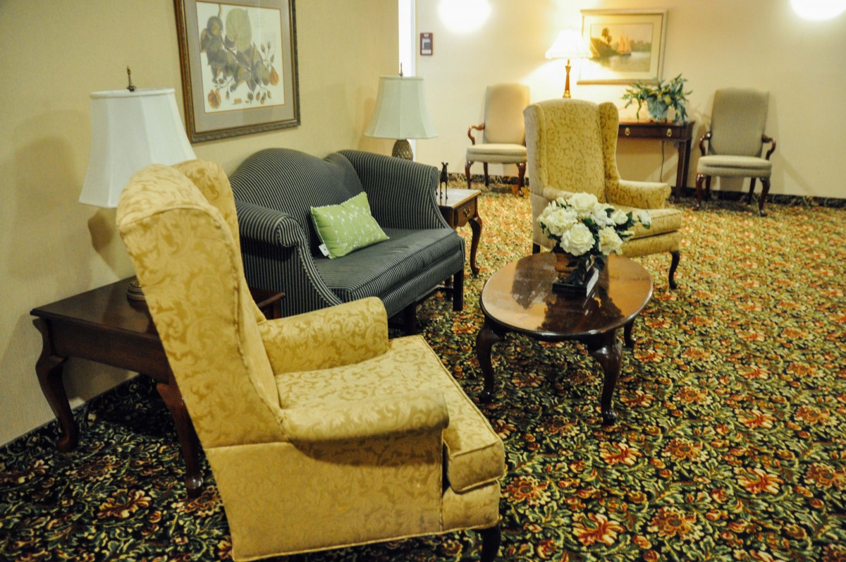 A cozy living room with vintage furniture, including a dark sofa, patterned armchairs, and a wooden coffee table on a decorative carpet.