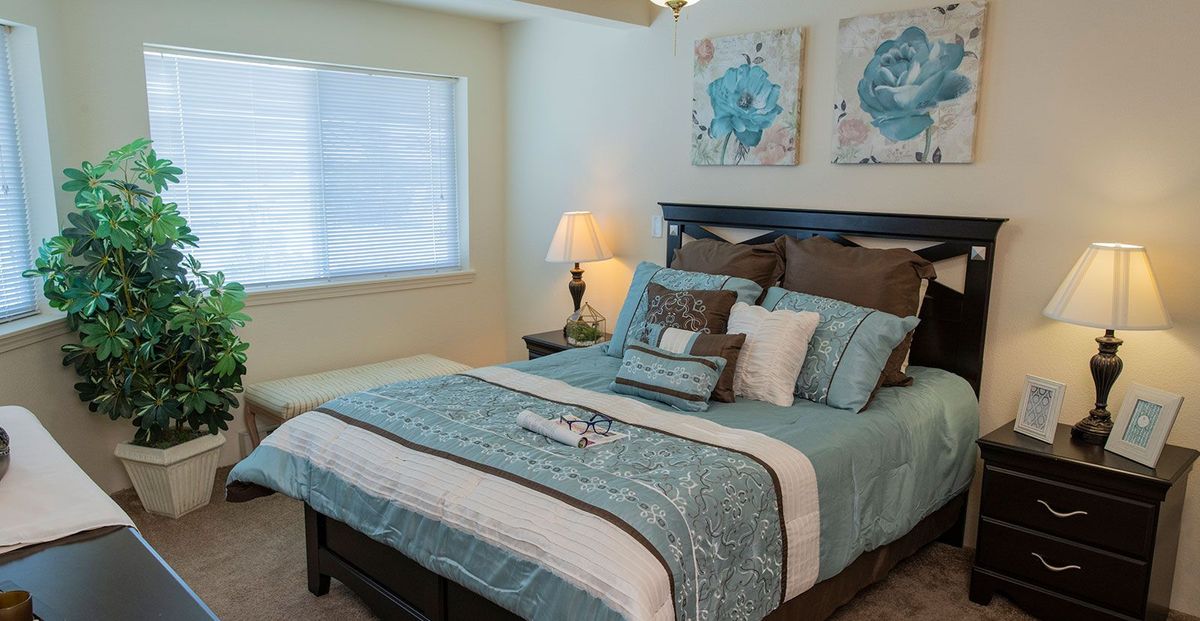 A cozy bedroom with teal and brown bedding, decorative pillows, and wall art.