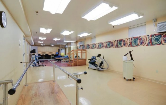 A spacious rehabilitation therapy room equipped with various exercise machines and parallel bars.