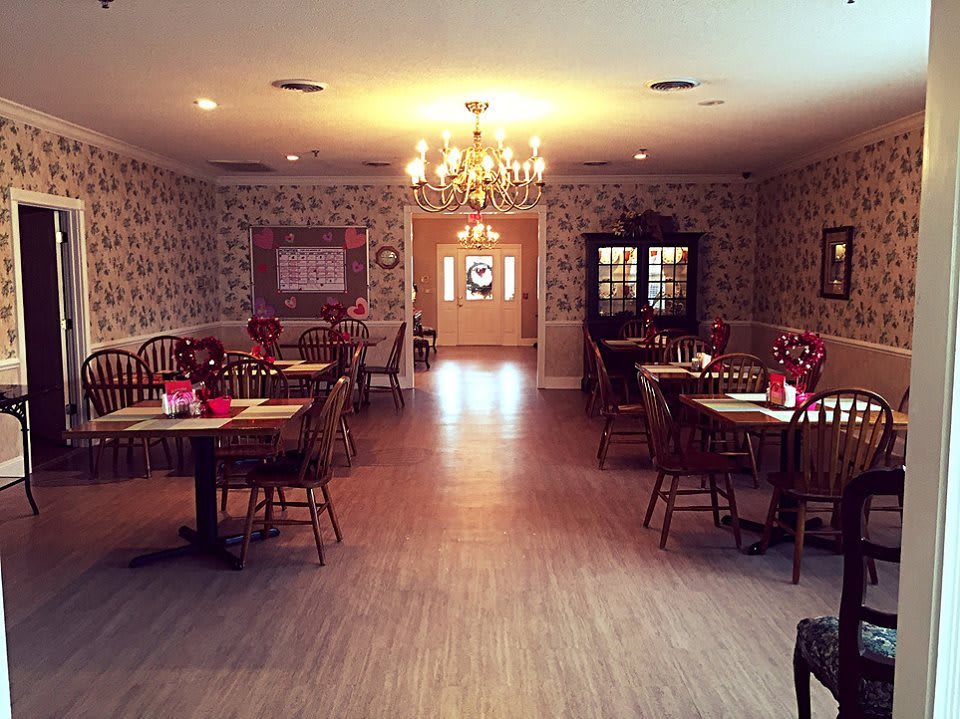 A warmly lit dining area with elegantly arranged tables and chairs, featuring a chandelier.