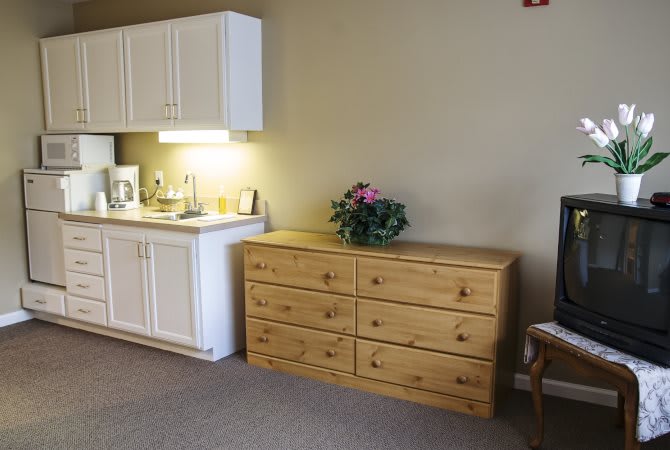 A cozy room interior featuring a wooden dresser and a small kitchenette with cabinets.