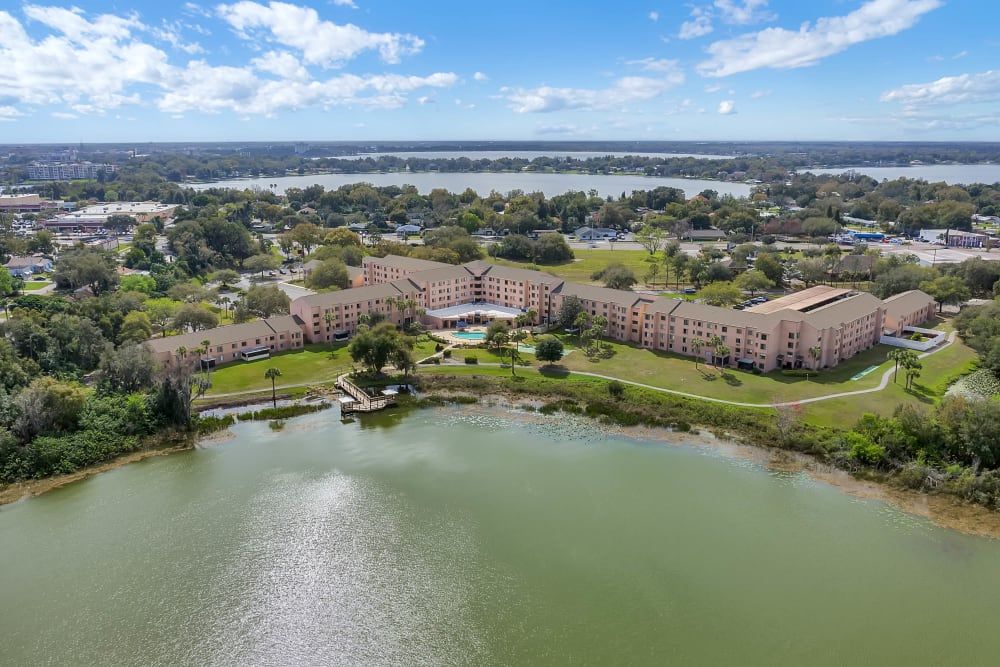 Aerial view of an apartment complex situated by a lake, with a cloudy sky in the background.