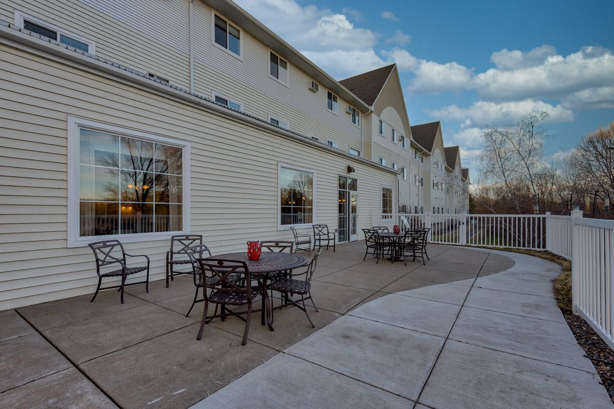 An outdoor patio area with tables and chairs alongside a building under a cloudy sky.