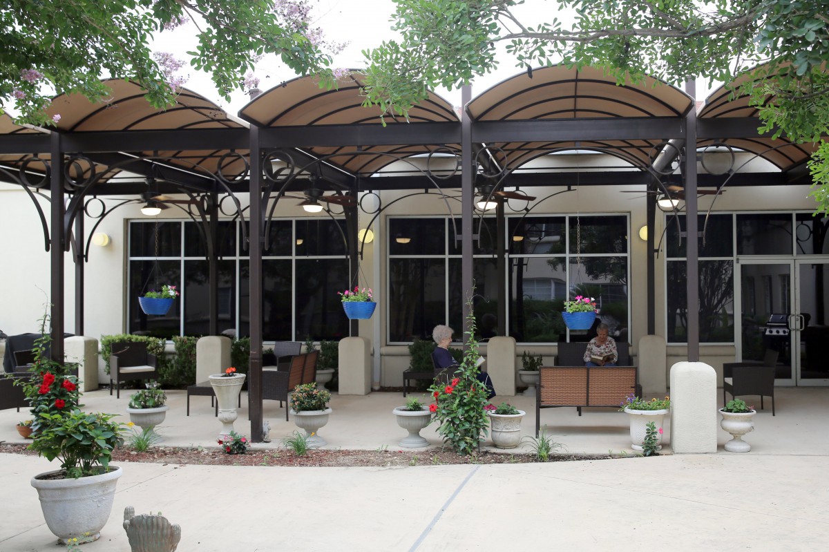 An outdoor cafe patio with covered seating areas surrounded by plants and trees.