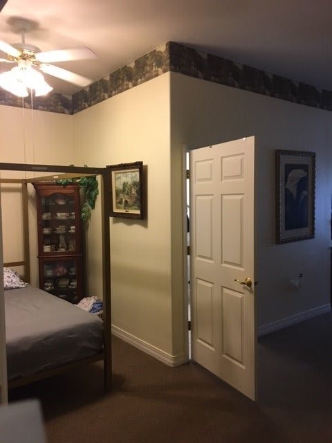 A cozy bedroom with a ceiling fan, open door, and wooden furniture.