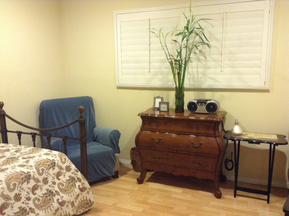 A cozy bedroom corner featuring a blue armchair, a wooden dresser with decorative items and a bamboo plant.
