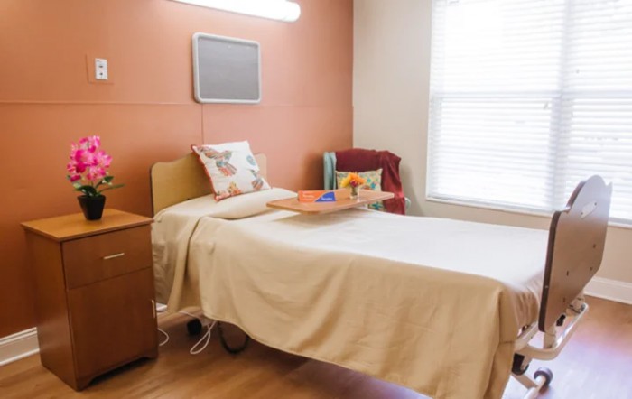 A hospital room with a bed, nightstand, and chair by the window.