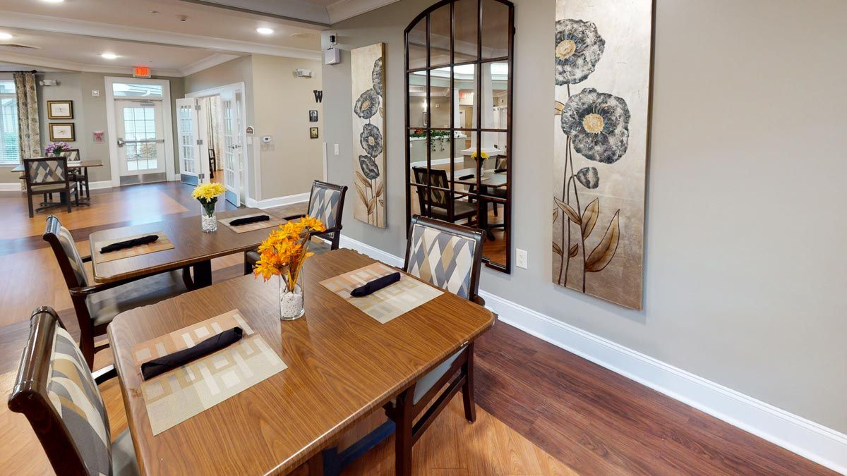 A cozy dining area featuring wooden tables and chairs, adorned with floral wall art and a large decorative mirror.