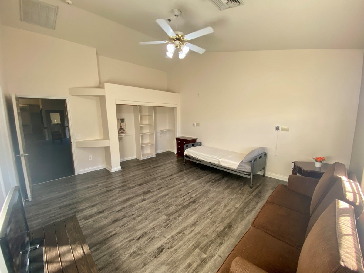 A spacious room with a bed, couch, and shelves, featuring a ceiling fan and wood flooring.