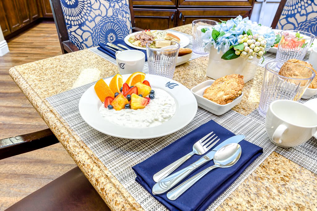 A beautifully arranged breakfast table featuring a bowl of yogurt with orange slices, blueberries, and peach slices, accompanied by a croissant and neatly set silverware.