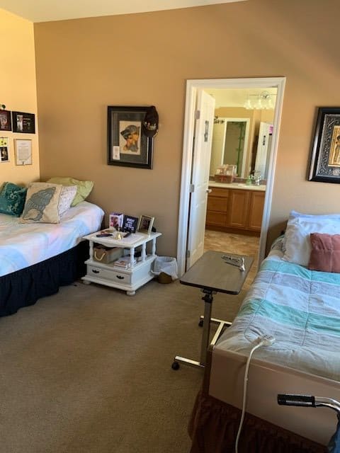 A cozy bedroom with two beds and a nightstand between them, leading into a bathroom through an open doorway.