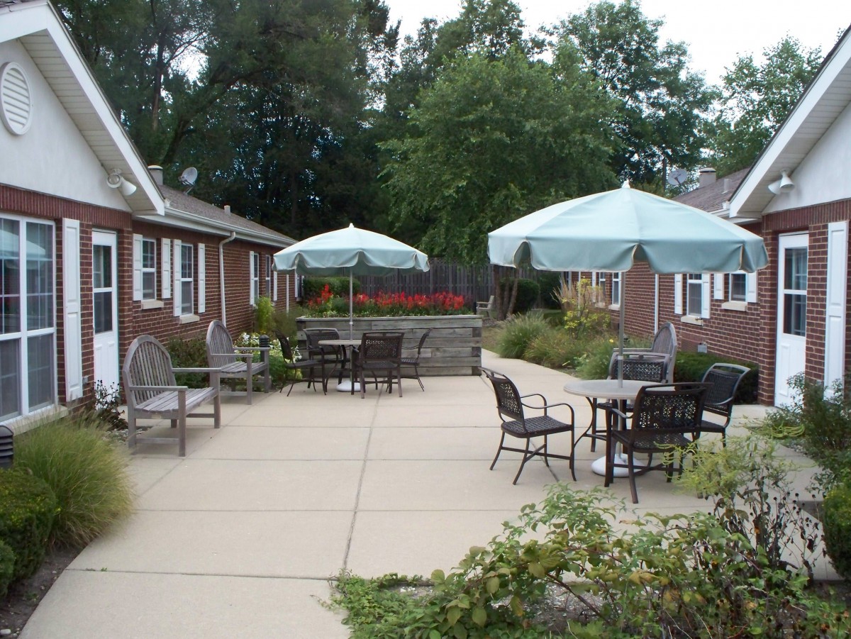 A cozy outdoor patio area with umbrellas and seating surrounded by brick buildings and greenery.
