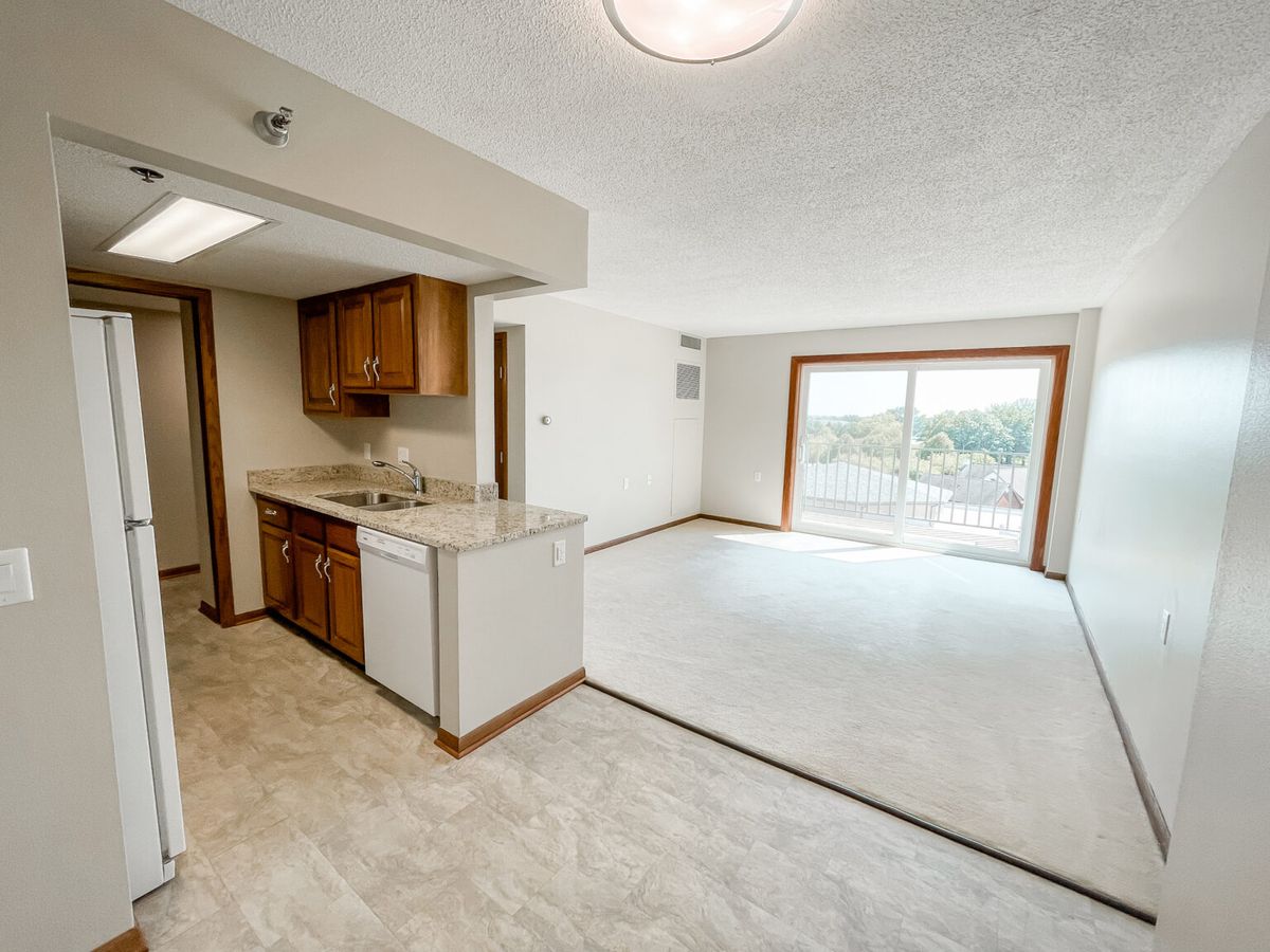 A bright apartment with an open floor plan, featuring a kitchen and living area with sliding doors leading to a balcony.