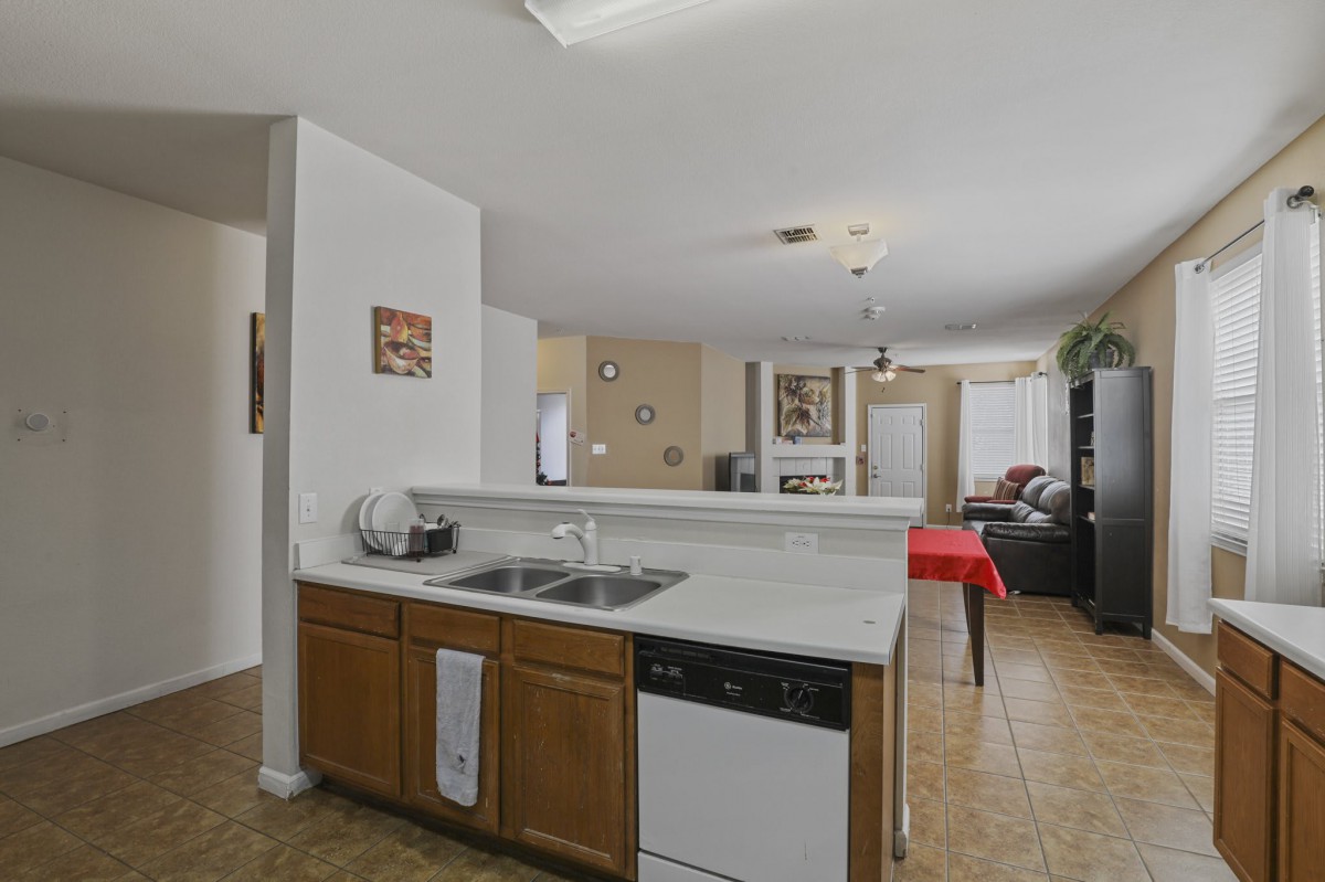 A cozy kitchen with wooden cabinets and a marble countertop, opening into a spacious living area.