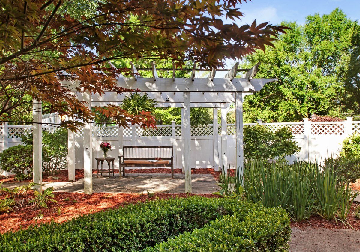 A peaceful garden with a white pergola, bench, and lush greenery.