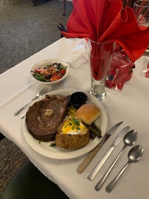 A delicious dinner spread featuring steak, a loaded baked potato, vegetables, a roll, and a fresh salad on a elegantly set table.
