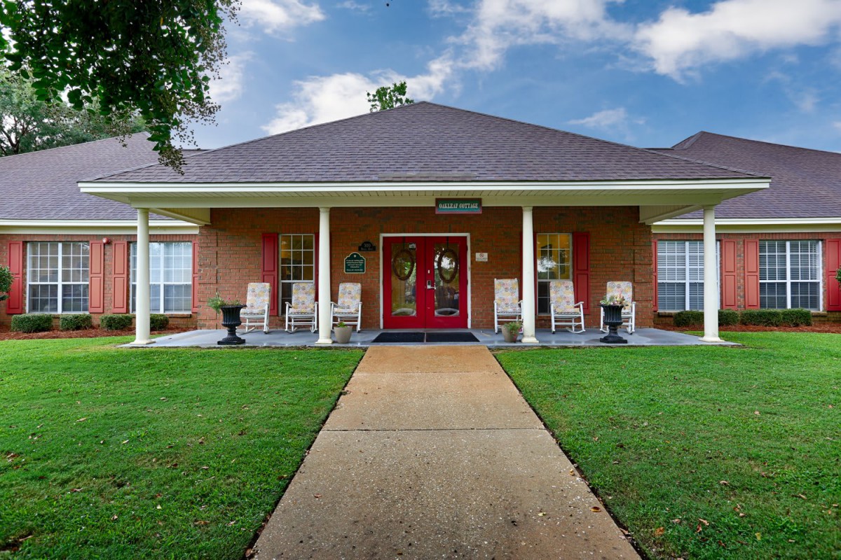 A welcoming house with a red door, white porch columns, and a green lawn under a cloudy sky.