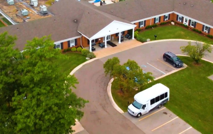Aerial view of a building with a driveway, parking lot, and a white van parked in front.