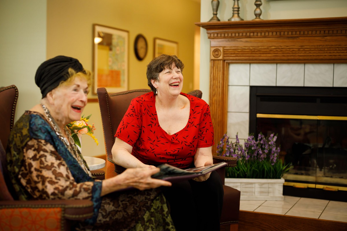 Two elderly women laughing and enjoying a conversation in a cozy living room.