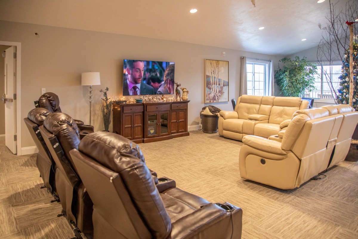 A cozy living room featuring recliner chairs and a sofa, with a large TV for home theater enjoyment.