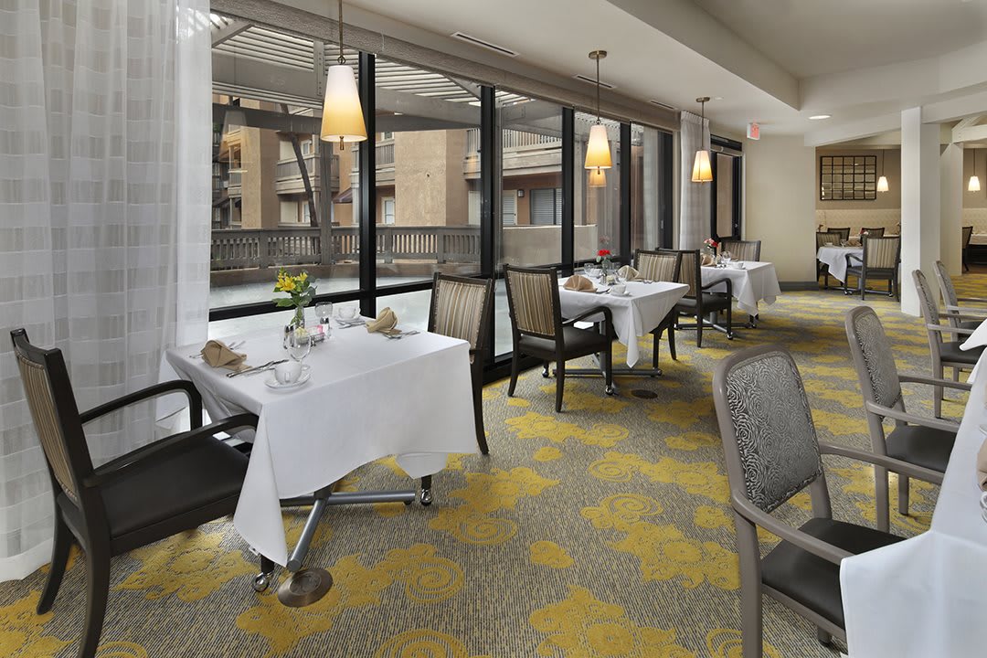 A modern dining area with neatly arranged tables and chairs, illuminated by natural light streaming through large windows.