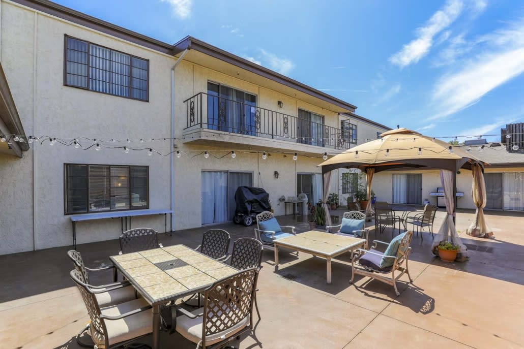 A spacious outdoor patio with tables, chairs, and umbrellas adjacent to a two-story building.