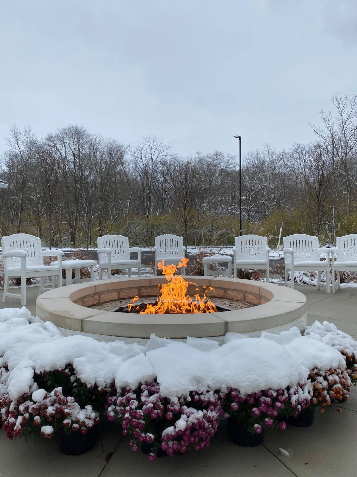 A cozy fire pit surrounded by snow-covered chairs on a chilly winter day.