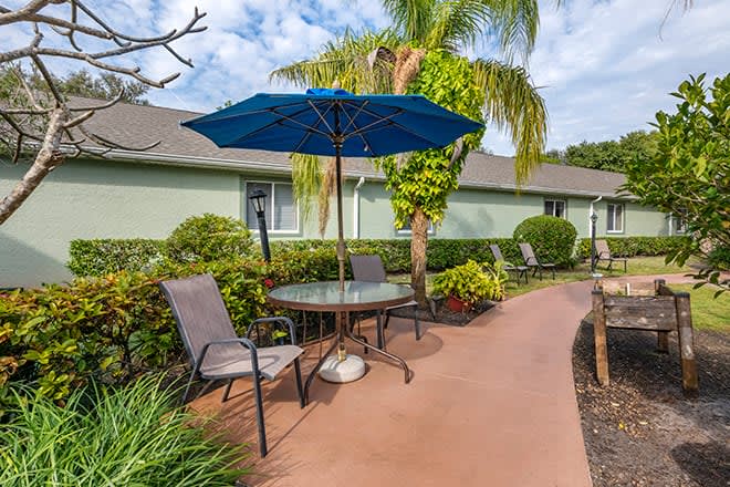 A serene patio area with a table, chairs, and an umbrella next to a garden pathway.