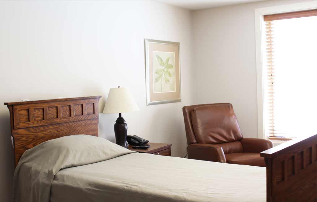 A minimalist bedroom with a bed, nightstand, lamp, and armchair.