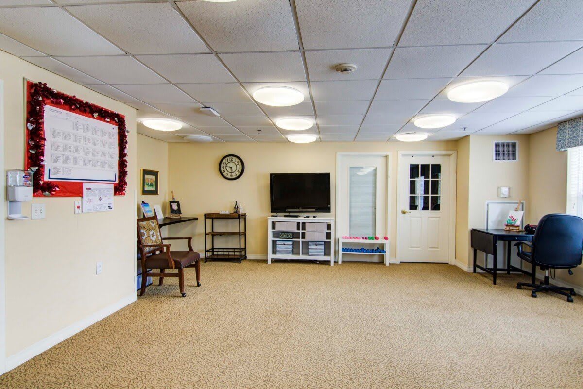 A spacious, carpeted room with a TV, shelves, chairs, and a clock on the wall.