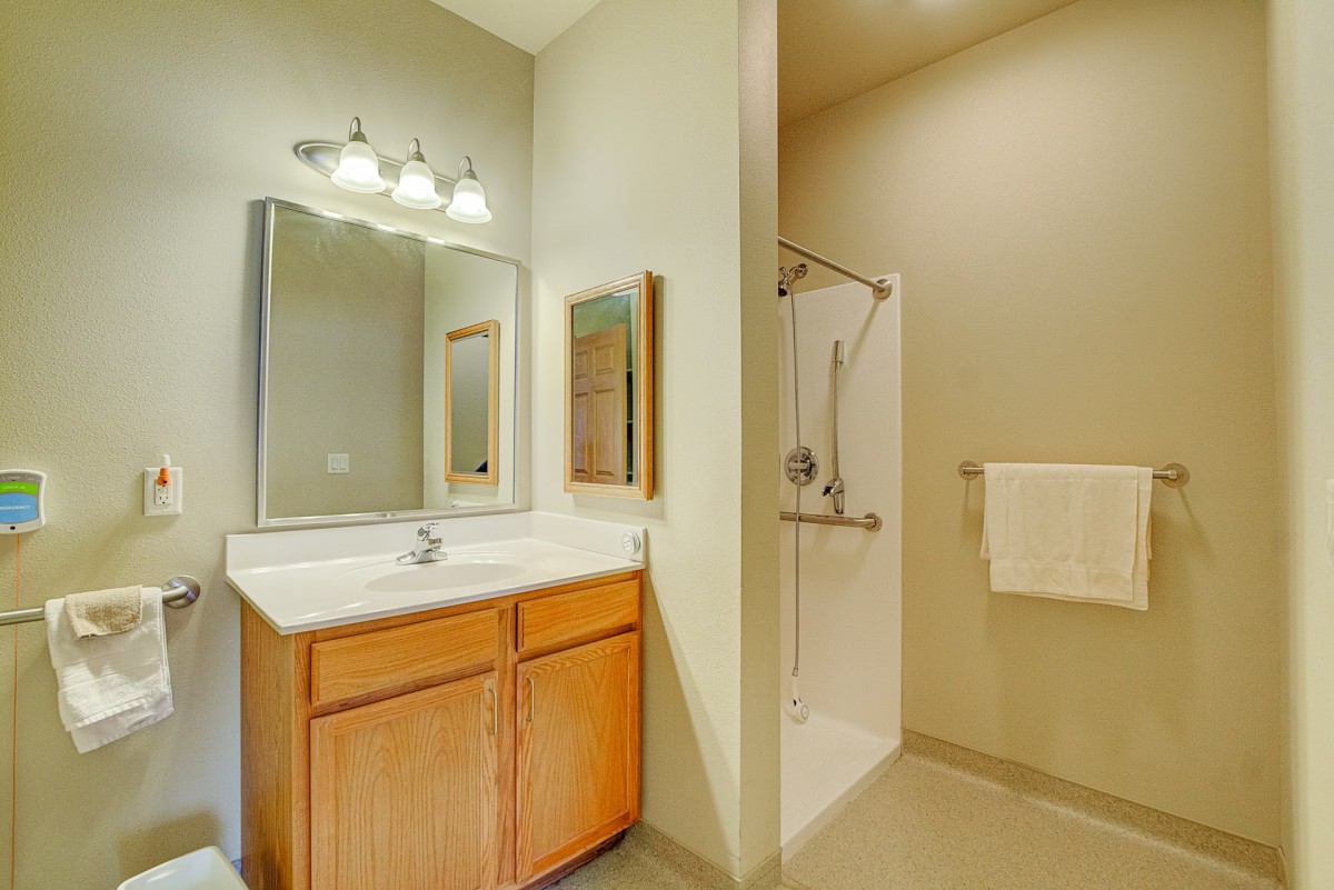 A clean and modern bathroom featuring a sink with a mirror, wooden cabinets, and a shower area.