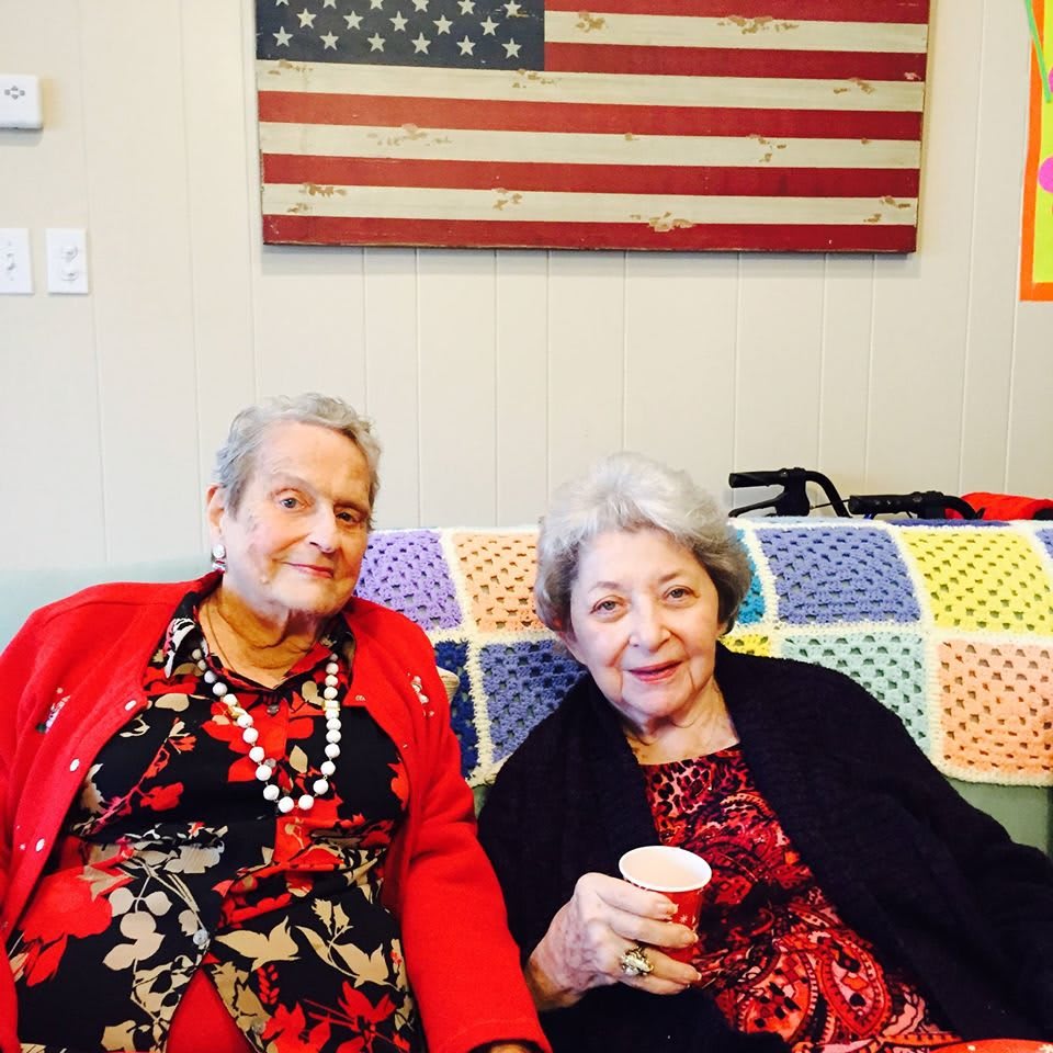 Two elderly women sitting together with an American flag in the background.