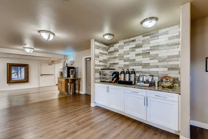 A modern kitchen interior with a coffee station, white cabinets, and wood flooring.