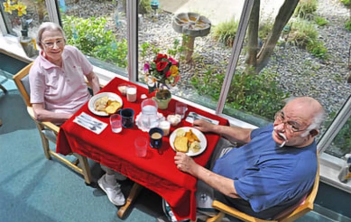 Two people enjoying a meal at a table with a red tablecloth next to large windows.