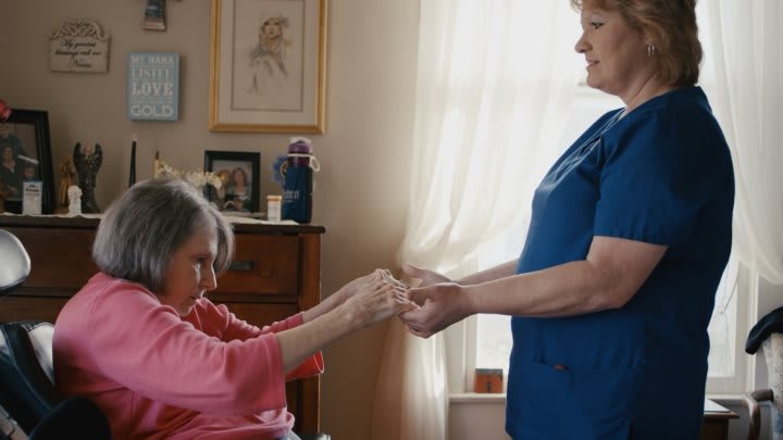 A nurse assists an elderly woman in a home care setting.