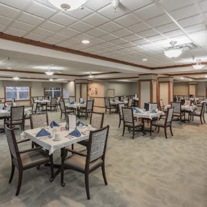 An elegant dining area with neatly arranged tables and chairs, featuring warm lighting and a carpeted floor.