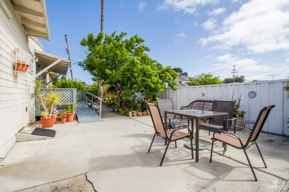 A sunny backyard patio with outdoor seating and lush green plants.