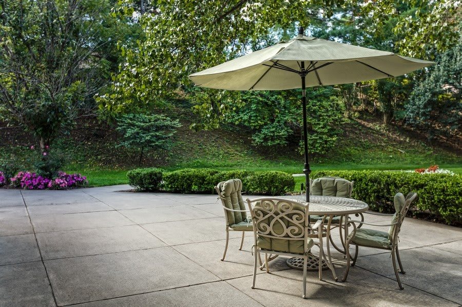 A peaceful outdoor patio with a table and chairs under an umbrella surrounded by lush greenery.