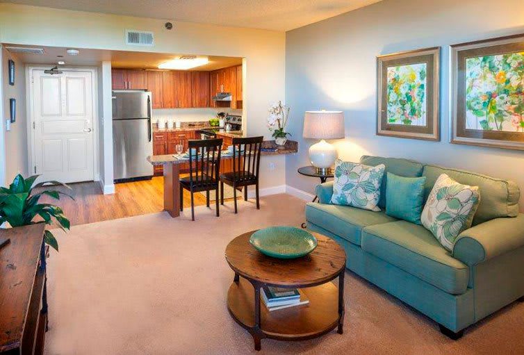 A modern open-concept living area features a cozy sofa, coffee table, and connected kitchen with wooden cabinets.