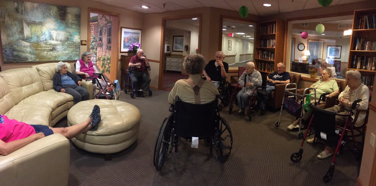 A group of elderly people sitting in wheelchairs inside a care home, engaged in a gathering.