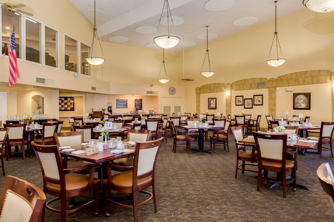 A spacious dining room with neatly arranged tables and chairs, softly lit by chandeliers.