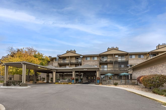 A front view of a hotel building with multiple stories, featuring a covered entrance and surrounded by trees under a partly cloudy sky.