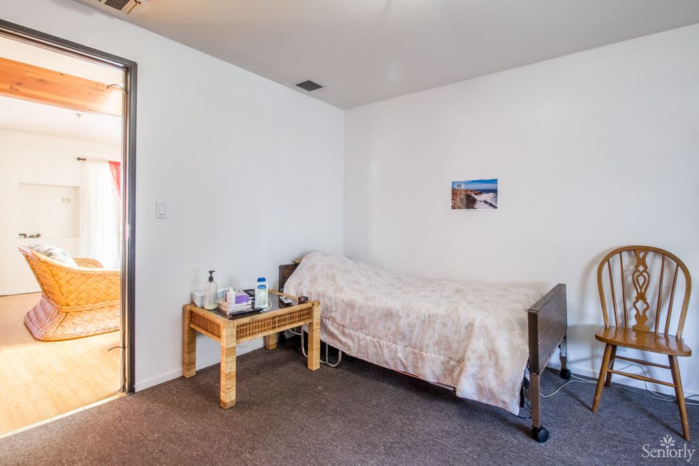 A minimalist bedroom with a single bed and a small side table on a carpeted floor.