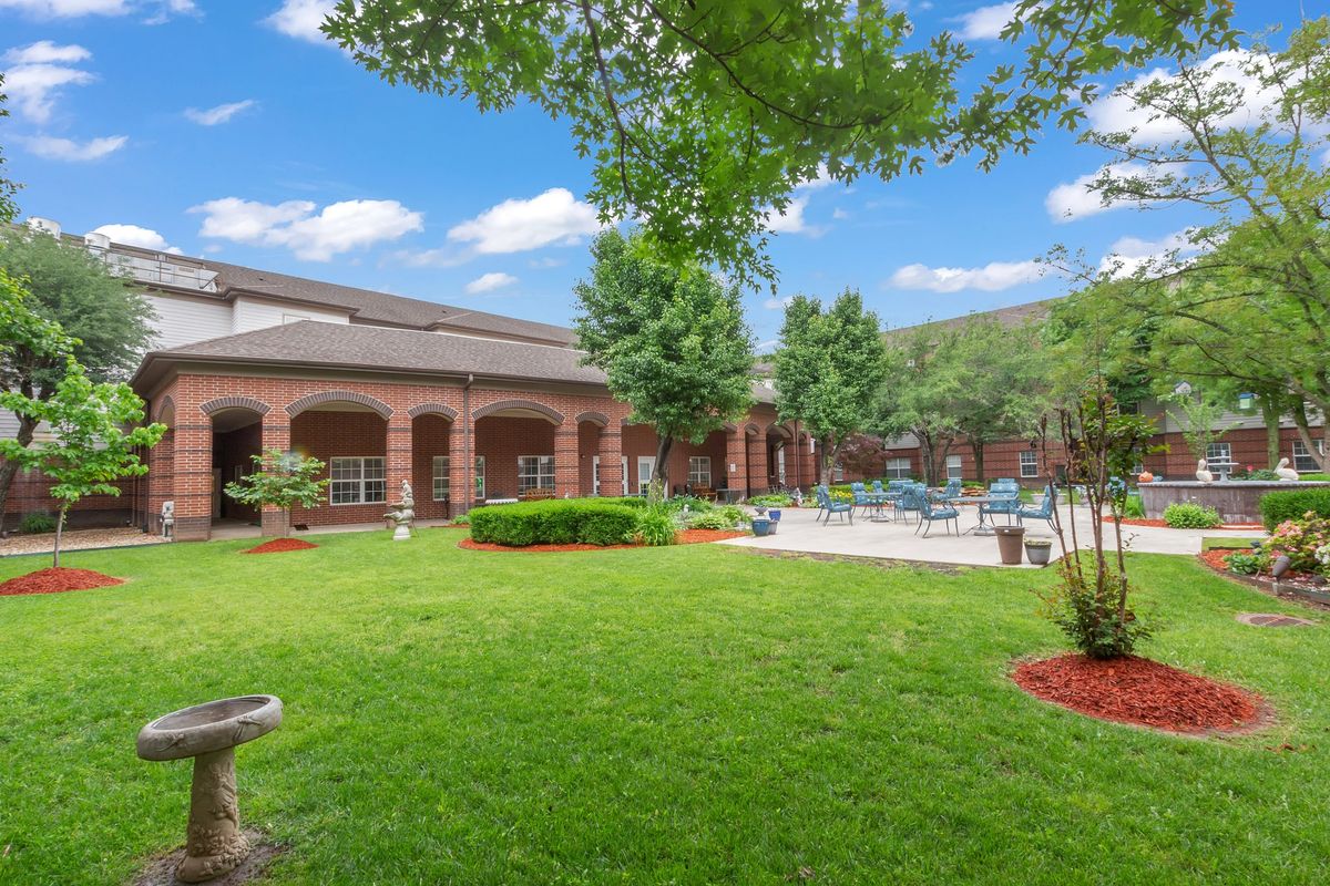 A scenic view of a building courtyard with lush green lawn, trees, and patio area.