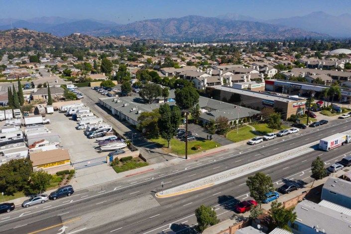 Aerial view of a suburban area with roads, buildings, and vehicles parked in lots, set against a backdrop of distant mountains.