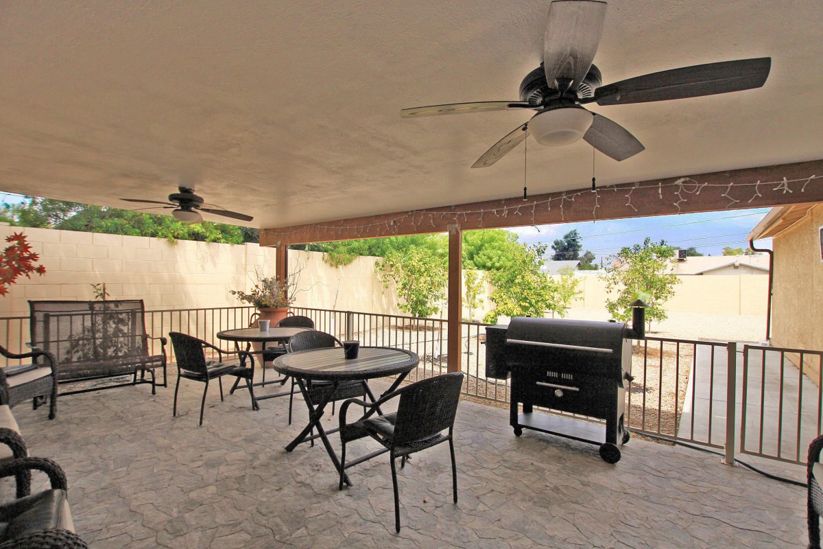 A spacious patio with ceiling fans, outdoor seating, and a grill in a backyard setting.