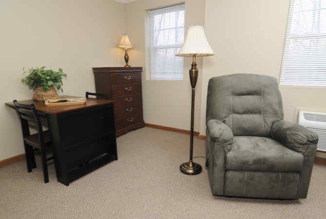 A cozy living room corner with an armchair, floor lamp, and dresser by the window.