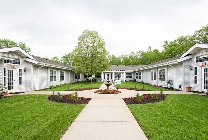 A serene courtyard with a central pathway surrounded by greenery and a building.