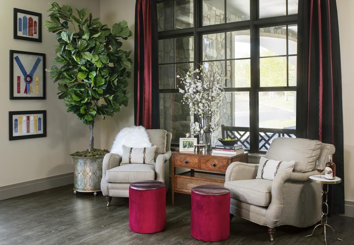 A cozy living room with armchairs, red stools, and a large window for natural light.