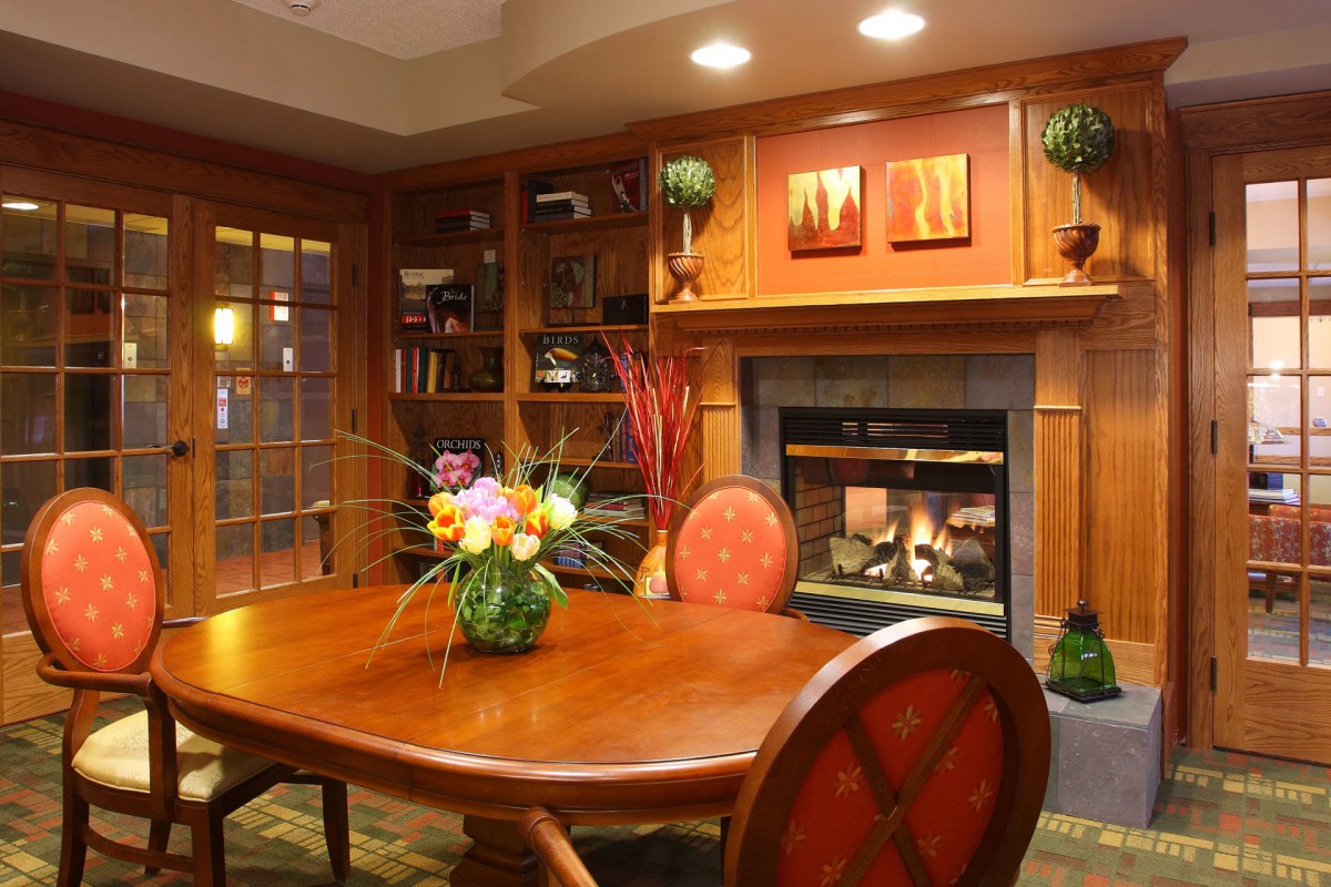 A cozy dining room with wooden furniture and a fireplace, adorned with bookshelves and floral decor.